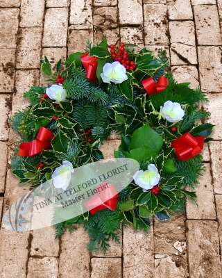 Festive wreath, adorned with white or red flowers, red berries, and bows. Vibrant greenery adds seasonal charm
