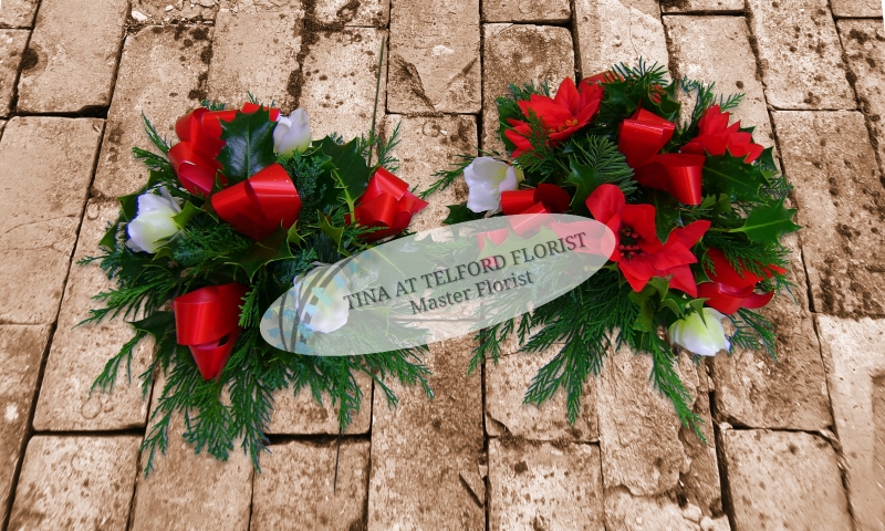 Festive posy arrangement with red ribbons and white flowers, surrounded by green foliage
