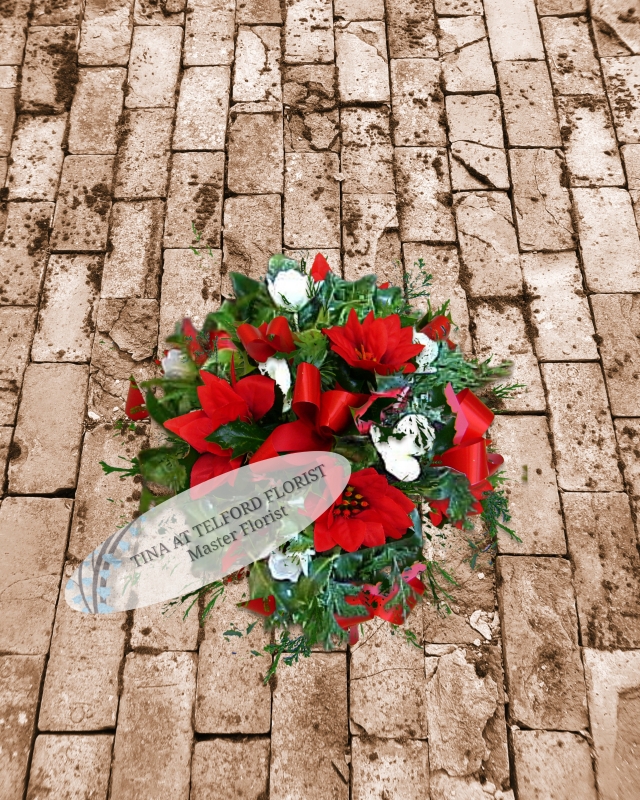 A holly posy arrangement with white flowers, greenery, and red ribbon