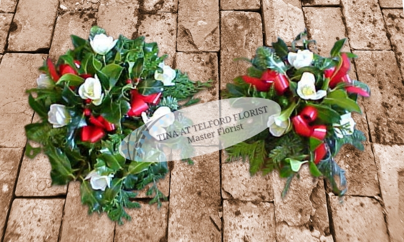 A holly posy arrangement with white flowers, greenery, and red ribbon