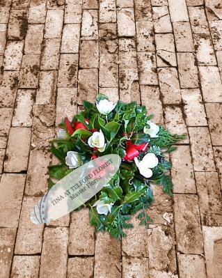 A holly posy arrangement with white flowers, greenery, and red ribbon