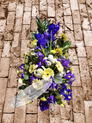 A vibrant floral funeral design featuring vivid blue and yellow flowers with lush green leaves funeral spray telford florist