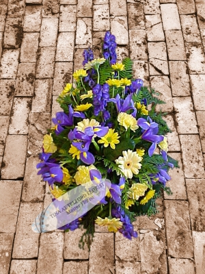 A funeral spray that features yellow and purple flowers with green foliage