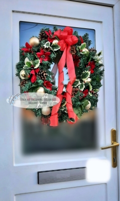 Festive Christmas wreath on a door with red ribbon, pinecones, and ornaments. Conveying holiday cheer and warmth