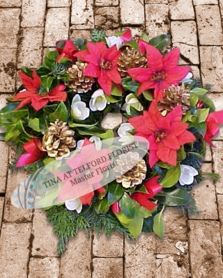 A holly wreath with red poinsettias, white flowers,gold  pine cones, and evergreen floiage
