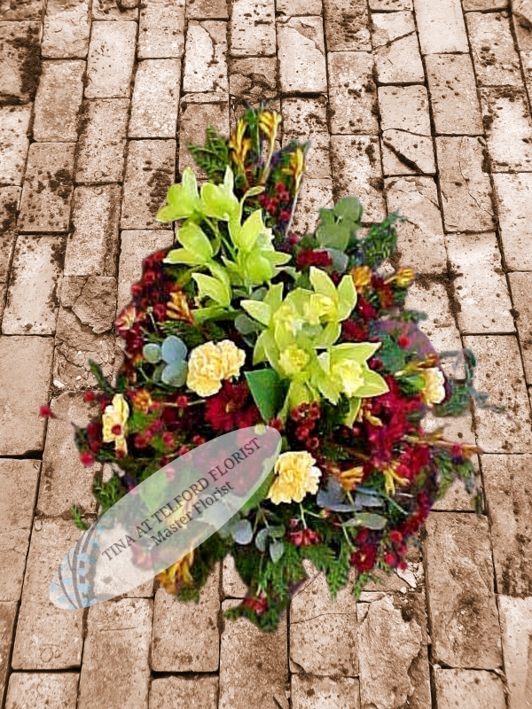 A bold funeral spray with green orchids, yellow carnations, and red flowers, exuding a natural, elegant feel, Telford Florist