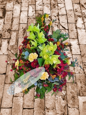 A bold funeral spray with green orchids, yellow carnations, and red flowers, exuding a natural, elegant feel, Telford Florist