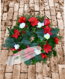 A festive wreath with holly leaves, red ribbons, and white flowers on a rustic stone background.