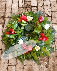 A festive wreath with holly leaves, red ribbons, and white flowers on a rustic stone background.