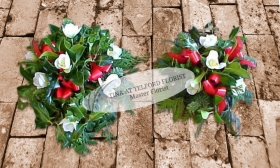A holly posy arrangement with white flowers, greenery, and red ribbon