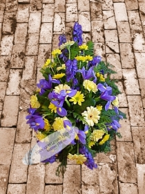 A funeral spray that features yellow and purple flowers with green foliage