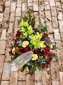 A bold funeral spray with green orchids, yellow carnations, and red flowers, exuding a natural, elegant feel, Telford Florist