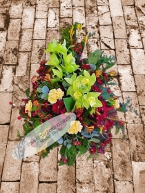 A bold funeral spray with green orchids, yellow carnations, and red flowers, exuding a natural, elegant feel, Telford Florist